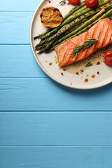 Tasty grilled salmon with tomatoes, asparagus and spices on light blue wooden table, top view. Space for text