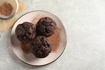 Delicious chocolate muffins and cacao powder on light grey table, flat lay. Space for text