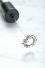 Black milk frother wand on white marble table, closeup