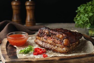 Piece of baked pork belly served with sauce and chili pepper on wooden table