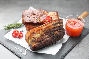  Pieces of baked pork belly served with sauce, rosemary and chili pepper on grey table © New Africa