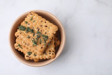 Cereal crackers with flax, sesame seeds and thyme in bowl on white marble table, top view. Space for text