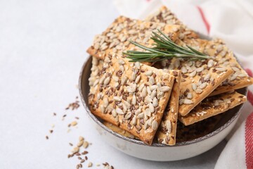 Cereal crackers with flax, sunflower, sesame seeds and rosemary in bowl on white table, closeup. Space for text