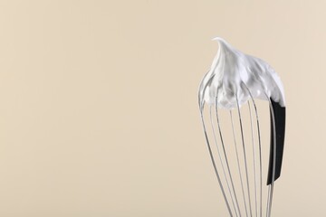 Whisk with whipped cream on beige background, closeup. Space for text