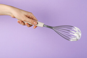Woman holding whisk with whipped cream on violet background, closeup