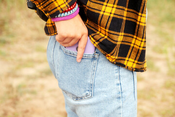 Woman puts mobile phone in jeans pocket on yellow nature background