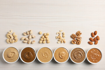 Many tasty nut butters in bowls and nuts on white wooden table, flat lay. Space for text