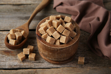 Brown sugar cubes in bowl and spoon on wooden table, closeup