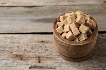 Bowl with brown sugar cubes on wooden table, closeup. Space for text