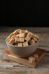 Brown sugar cubes in bowl on wooden table, closeup