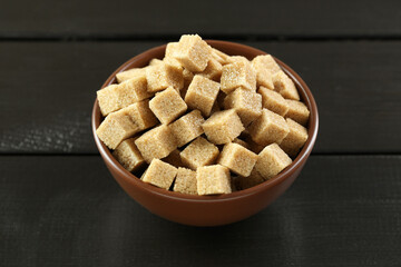 Brown sugar cubes in bowl on black wooden table, closeup
