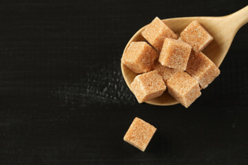 Brown sugar cubes in spoon on black wooden table, closeup. Space for text