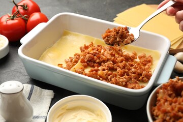 Woman making lasagna at dark table, closeup