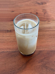 Glass of milk on wooden table. Iced coffee on an acacia wood table. Cold brew. Plant-based latte in the cup with ice cubes.