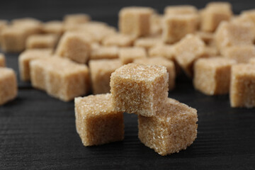Brown sugar cubes on black wooden table, closeup