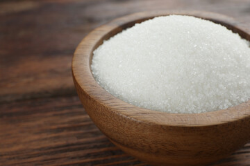 Granulated sugar in bowl on wooden table, closeup. Space for text