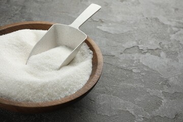 Granulated sugar in bowl and scoop on grey textured table, closeup. Space for text