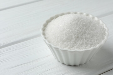 Granulated sugar in bowl on white wooden table, closeup. Space for text
