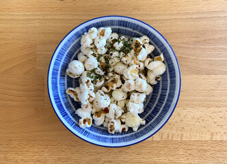 Popcorn in bowl. Healthy seasoned snack in a blue and white porcelain bowl. Popcorn served on a wooden table.
