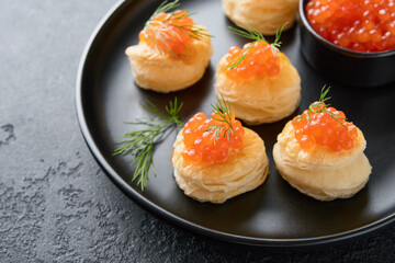 Salmon red caviar toast. Christmas canape or toast with red caviar on black plate on dark background. Idea to xmas snack. Gourmet food. Texture of caviar. Seafood.