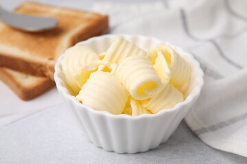 Tasty butter curls in bowl and toasts on light grey table, closeup