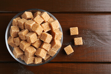 Brown sugar cubes in glass bowl on wooden table, top view