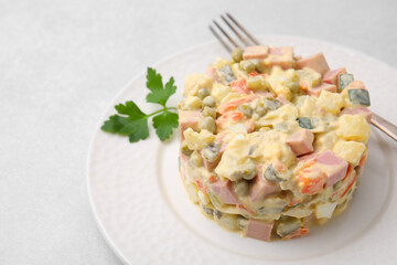 Tasty Olivier salad with boiled sausage and fork on light table, closeup. Space for text