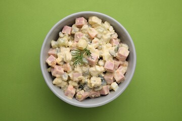 Tasty Olivier salad with boiled sausage in bowl on green table, top view