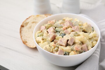 Tasty Olivier salad with boiled sausage in bowl on white table, closeup. Space for text