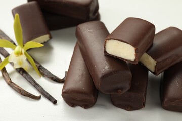 Glazed curd cheese bars, vanilla pods and flower on white table, closeup