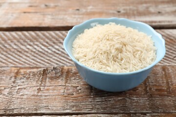 Raw basmati rice in bowl on wooden table, space for text