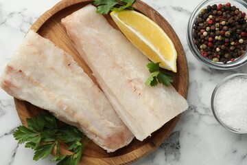 Fresh raw cod fillets, spices and lemon on white marble table, flat lay