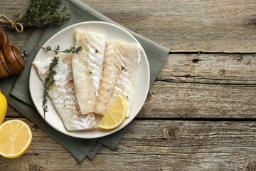 Fresh raw cod fillets with thyme and lemon on wooden table, flat lay. Space for text