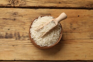 Raw basmati rice in bowl and scoop on wooden table, top view