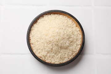 Raw basmati rice in bowl on white tiled table, top view