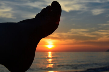 stopa i zachód słońca nad morzem, relaks na plaży o zachodzie słońca, foot, relaxing on the beach at sunset, foot against the background of the setting sun, vacation	
 - obrazy, fototapety, plakaty