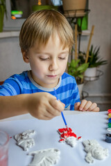 The kid draws and paints plaster figures with a brush and gouache on a piece of paper.