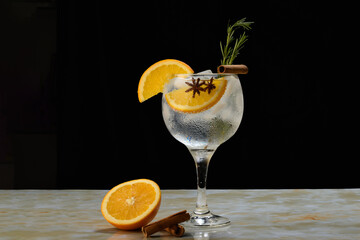 Gin and tonic cocktail with orange, cinnamon, rosemary and star anise on a black background