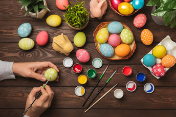 Woman paints Easter eggs at the kitchen wooden table.Happy Easter celebration concept.Colorful...