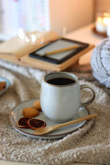 Cup of tea or coffee, cookies, books, glasses, e-reader, almonds, ball of yarn, knitting needles and lit candles on the table. Hygge at home. Selective focus.