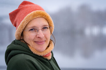 Happy woman in her early 50s outside in cold weather with light snow falling. Plenty of room for copy on right.