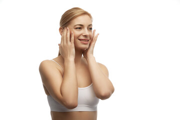 Fototapeta premium Portrait of young attractive woman in white underwear doing facial massage against white studio background. Anti-aging procedures. Concept of natural beauty, spa, cosmetology, female health. Ad