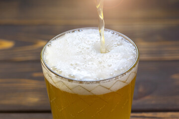 Pouring liquid gold-yellow beer with white foam into a glass. Close up view.
