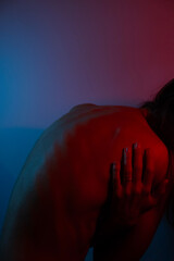 Intense young woman, blue and red lighting on back. Neck and back pain.Mental burden concept.
Bent woman with bare back