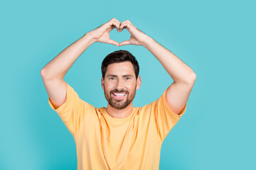 Fototapeta na wymiar Photo of young friendly handsome model guy wear yellow t shirt demonstrate appreciation heart figure isolated on cyan color background