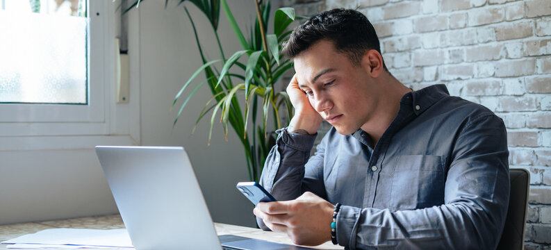 Unhappy young man looking at phone, feeling nervous of bad device work, internet disconnection, lost data or inappropriate online content. Anxious male user dissatisfied with application or service..