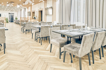 Side view of a large empty bright restaurant with tables, soft chairs, curtains and a wooden floor. Modern interior of a cafe, restaurant for events, holidays, weddings, birthdays with copy space.