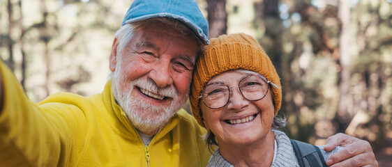 Head shot portrait close up of cute couple of old seniors taking a selfie together in the mountain forest looking at the camera smiling having fun enjoying. Two mature people hiking. - Powered by Adobe