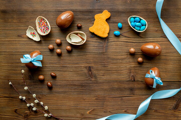 Chocolate Easter eggs in blue ribbon and bunny cookies on wooden background