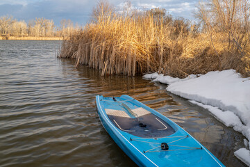 Naklejka na ściany i meble touring stand up paddleboard with a safety leash on a shore of lake in northern Colorado, winter or early spring scenery with some snow